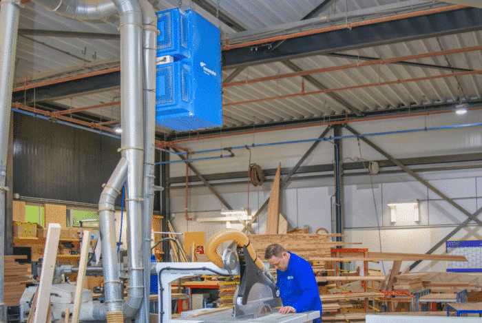 Houtbewerkingswerkplaats met werknemer en luchtreiniging voor vermindering van houtstof